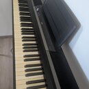 Černé digitální piano s klávesnicí. Na korpusu je bílý nápis KORG a modelové označení SP-170S. Nástroj je vybaven černým hudebním stojanem na noty. P…