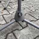 Detail spodní části šedého kovového stativu s třemi nohama. Na centrálním plastovém spoju je umístěno kulaté logo s nápisem K&M. Povrch plastu a kovo…