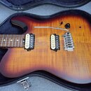 Elektrická kytara s trupem v barvě sunburst a viditnou strukturou dřeva, umístěná v černém tvrdém kufru. Nástroj má dva snímače typu humbucker, chrom…