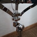 Detailní záběr na chromovaný kovový stojan. Jsou vidět nastavitelné klouby, šrouby a teleskopický mechanismus. Povrch je lesklý, bez viditelných znač…