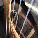 Detailní pohled na zvukovou otvory akustické kytary s viditelnými strunami. Vzadu v korpusu jsou vidět dřevěné rozpěry a struktura dřeva. Povrch kyta…