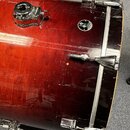 Detailní pohled na červený lakovaný basový buben s kovovými obručemi a lugy. Na korpusu je umístěna malá kulatá nálepka s nápisem "Premier DRUMMER".…