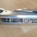 Stříbrná kovová svorka s nápisy FastClamp a TAMA. Povrch vykazuje drobné škrábance a známky používání. Předmět má protáhlý tvar s několika pohyblivým…