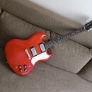 Červená elektrická kytara s bílým pickguardem a dvěma humbuckery. Na hlavě hmatníku je viditelné logo Epiphone. Nástroj vykazuje známky běžného použí…
