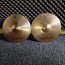 Dvě mosazné činely s viditelným opracováním povrchu. Oba mají v dolní části nápis istanbul Agop Made in Turkey. Levý činel má navíc v horní části tro…