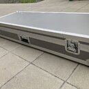 Šedý transportní kufr s hliníkovými hranami a kovovými rohy. Na straně jsou umístěny tři kovové zámky a jedna rukojeť. Povrch kufrů je hladký, bez vi…