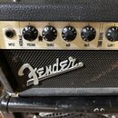 Detailní pohled na ovládací panel kytarového komba značky Fender. Na zlatovém panelu jsou nápisy INPUT, NORMAL (VOLUME, TREBLE, MID, BASS) a TUBE DRI…