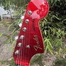 Červená hlava elektrické kytary s chromovanými ladičkami. Na povrchu je bílý nápis Fender JAGUAR a pod ním menší text MEXICO. Lak je glossy s viditel…