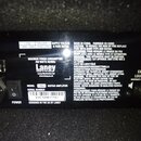 Fotografie detailu zadní strany kytarového komba s černým povrchem. Je zde viditelný štítek se značkou Laney a nápisem POWER TO THE MUSIC, model RB8…