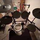 Elektronická bicí souprava s černými pady a činely na kovovém stojanu. Na bílém snare padu je vidět nápis Roland. Soubor obsahuje pět padů a dva čine…