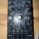 Modulární syntetizátor v tmavě šedé barvě s nápisem WAVES v horní části a behringer ve spodní. Zařízení obsahuje několik otočných potenciometrů s pop…