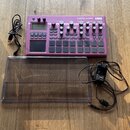 Fialový sampler s nápisy electribe sampler a KORG. Zařízení obsahuje displej, několik otočných knoflíků a mřížku s čtvercovými padovými tlačítky. K p…