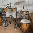 Elektrická nebo hybridní bicí souprava s dřevěnými korpusy v přirozené barvě. Na bubnech jsou vidět nápisy "Laguna". Souprava obsahuje čtyři bubny, d…