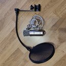 Sada pro nahrávání složená z kondenzátorového mikrofonu stříbrné barvy, popfiltru a držáku s pružinovým العنastem. Na těle mikrofonu je nápis „ap a43…