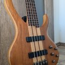 Detailní pohled na tělo a hmatník čtyřstrunné basové kytary z přírodního dřeva s viditným sletováním různých odstínů. Nástroj má dva černé snímače a…
