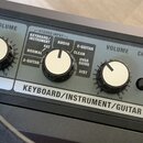 Detailní pohled na ovládací panel černého zesilovače s několika ovládacími knoflíky. Na panelu jsou nápisy VOLUME, MIC a KEYBOARD/INSTRUMENT/GUITAR.…
