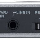 Detailní pohled na horní panel stříbrného elektronického zařízení s černým ovládacím polem. Jsou zde vidět vstupy s nápisy GUITAR/ MIC IN a LINE IN,…