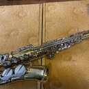 Mosazný saxofon s lesklým zlatým povrchem. Na korunu nástroje je vyryt nápis "The King" a dále "Super 20". Nástroj vykazuje drobné známky opotřebení…