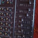Černý míchací pult s řadou vertikálních posuvníků a zahlreichen otočnými knoflíky. Na panelu jsou vidět bílé nápisy jako STEREO MASTER, BUS OUT, SOLO…