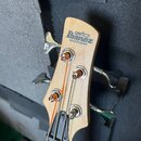 Detail hlavy basové kytary z přírodního světlého dřeva. Na hlavě je modrý nápis Ibanez a pod ním menší černý text SOUNDGEAR a logo GIO. Nástroj má čt…