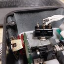 Detailní pohled do otevřeného černého plastového šasi elektronického zařízení. Uvnitř jsou vidět zapájené součástky, zelený plošný spoj a bílé vodiče…