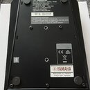 Fotografie zachycuje spodní stranu černé míchací konzole. Na horní části je bílý štítek s nápisy YAMAHA, MIXING CONSOLE MODEL MG06, МИКШЕРНАЯ КОНСОЛЬ…