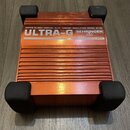 Oranžový kovový přístroj s černými gumovými nožičkami na rozích. Na horní části je bílý nápis ACTIVE DI-BOX/VIRTUAL 4x12" CABINET SIMULATION MODEL GI…