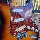 Elektrická kytara s trupem v barevném přechodu od žluté přes oranžovou k hnědé. Nástroj má hnedý mramorovaný pickguard, tři bílé snímače a javorový h…