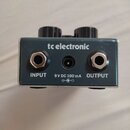 Kryt efektového pedálu v modré barvě s kovovým rámem. Na povrchu je bílý nápis tc electronic a označení vstupů INPUT, OUTPUT a 9 V DC 100 mA s ikonou…