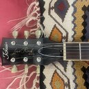 Detail hlavy černé elektrické kytary s bílými nápisy „Tokai“ a „Love Rock MODEL“. Na hlavě jsou vidět stříbrné ladičky s bílými plastovými knoflíky.…