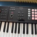 Černý klávesový nástroj s bílými a černými klávesami. Horní panel obsahuje sekce s nápisy ARP/RHYTHM, SEQUENCER a SAMPLER, digitální displej s číslem…
