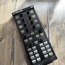 Černý DJ kontrolér s nápisy TRAKTOR a KONTROL X1. Zařízení obsahuje několik řad knofíků, posuvníků a bílých tlačítek s popisky jako DELAY, REVERB, FI…