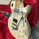 Elektrická kytara krémové barvy s bílým pickguardem v otevřeném kufru s červenou výstlkou. Nástroj má dva snímače typu humbucker, pětiknobovkové ovlá…