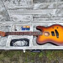 V otevřeném tvrdém kufru leží akustická kytara s Tobacco Sunburst barevným přechodem a hnědým hmatníkem. K nástroji je přiložen černý instrumentální…