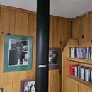 Černý sloupový reproduktor potažený látkovou textilem. V dolní polovině je bílý nápis BOSE. Reproduktor stojí v prostoru s dřevěným obkladem stěn a p…