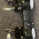 Černý kovový svorkovací adaptér se dvěma stahovacími mechanismy a stříbrnými knoflíky. Na povrchu nejsou vidět žádné značky, loga ani nápisy. Lak je…