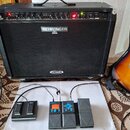 Černý kytarový kombozesilovač s nápisy BEHRINGER a V-TONE. Před zesilovačem jsou umístěny tři efektové pedály: černý pedál s nápisy EFFECT a SUSTAIN,…