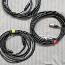 Tři srolovaný černé audio kabely. Dva z nich mají koncovky typu XLR, jeden má jednu koncovku typu jack. Kabely jsou stahovány barevnými suchými staho…