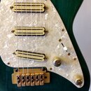 Detail elektrické kytary s tmavě zeleným povrchem a bílým perleťovým pickguardem. Nástroj má tři humbuckerové snímače s krémovými kryty, přičemž na s…