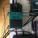 Zelený efekt pedál značky boss s nápisem Slicer SL2. Na zařízení jsou ovládací knofíky a přepínače s popisky jako TEMPO, DUTY, VARI a CHECK. Pedál je…