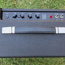 Kytarový kombozesilovač v černém texturovaném potahu s černým ovládacím panelem. Na panelu jsou nápisy INPUT, GAIN, TONE, REVERB, MASTER, STUDIO 10 E…
