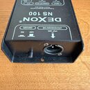 Černý kovový DI box s nápisy DEXON®, NS 100 a Professional Single-Channel Passive Direct Box. Na horní straně jsou označení INPUT (50k ohm), PARALLEL…
