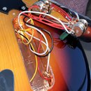 Fotografie zachycuje zadní část elektrokitary s otevřenou dutinou pro elektroniku. V dutině je vidět měděné stínění a svazek červených, bílých, žlutý…
