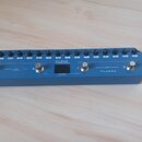 Modře šedý efektový pedál s kovovým povrchem. Na horní části je řada černých tlačítek a pod nimi nápisy: MASTER, LEVEL, REVERB, TIME, DELAY, RATE, MO…