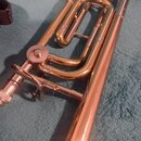 Detailní pohled na část trubky s mosazným povrchem. Jsou vidět ventily, ladicí tahy a mechanismus s pružinou. Na nástroji nejsou žádné viditelné znač…
