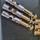 Tři kovové ventily z mosazi a nerezové oceli s vyfrézovanými otvory. Jsou umístěny na černém povrchu z umělé kůže s logem Yamaha v dolní části. Povrc…