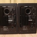 Dva černé studiové reproduktory z pohledu zadní strany. Na obou je nápis POWERED SPEAKER SYSTEM MODEL HS7 a logo YAMAHA. Levý reproduktor má uvedeno…