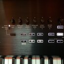 Detailní pohled na ovládací panel černého klávesového nástroje. Panel obsahuje řadu otočných potenciometrů s popisky: 1 CUTOFF GATE, 2 RESONANCE VELO…