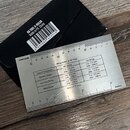 Kovové pravítko s tabulkou pro nastavení výšky strun. Na nástroji je nápis „String Action at 12th Fret“ a tabulka s hodnotami pro „Electric Guitar“,…