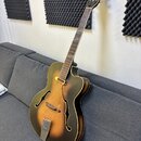Polodubová elektrická kytara s tmavě hnědým přechodem (sunburst) a krčkem z tmavého dřeva. Na hlavě je viditelné logo s nápisem "Epiphone". Tělo má d…